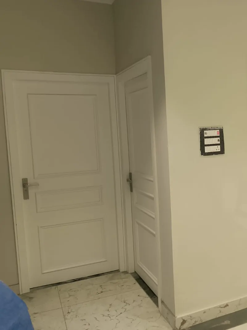 Two white raised-panel doors meeting at a corner beside a switchboard, on a marble floor